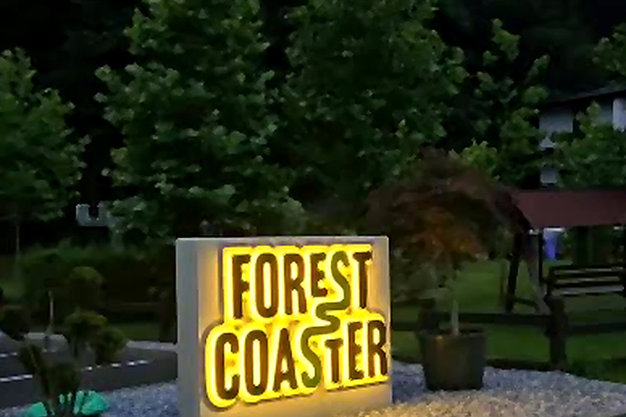 Das beleuchtete Forest-Coaster-Schild am Eingang, in der Dämmerung