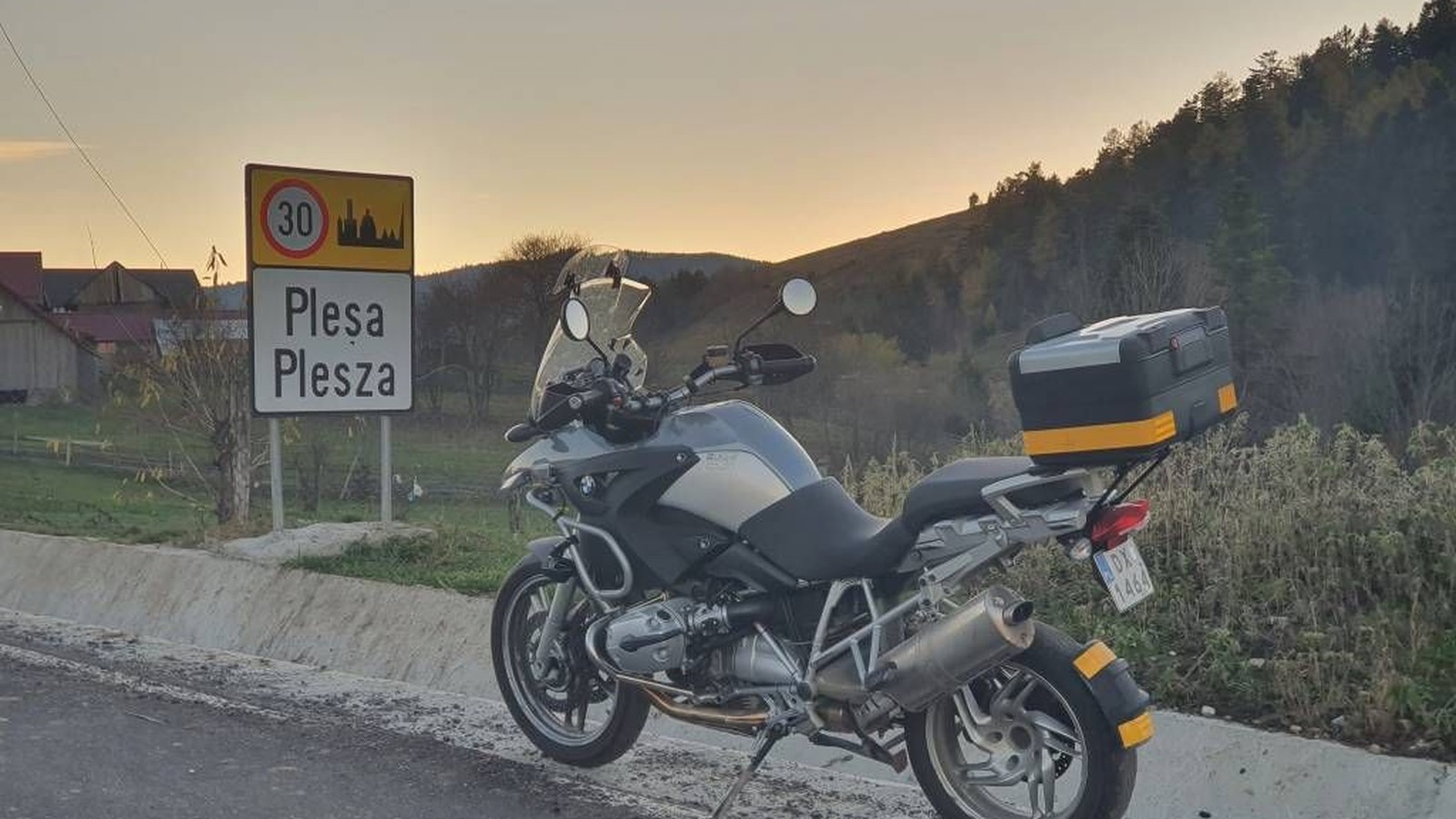 Motocykl przy tablicy z dwujęzyczną nazwą wsi: Pleșa i Plesza, o zachodzie słońca