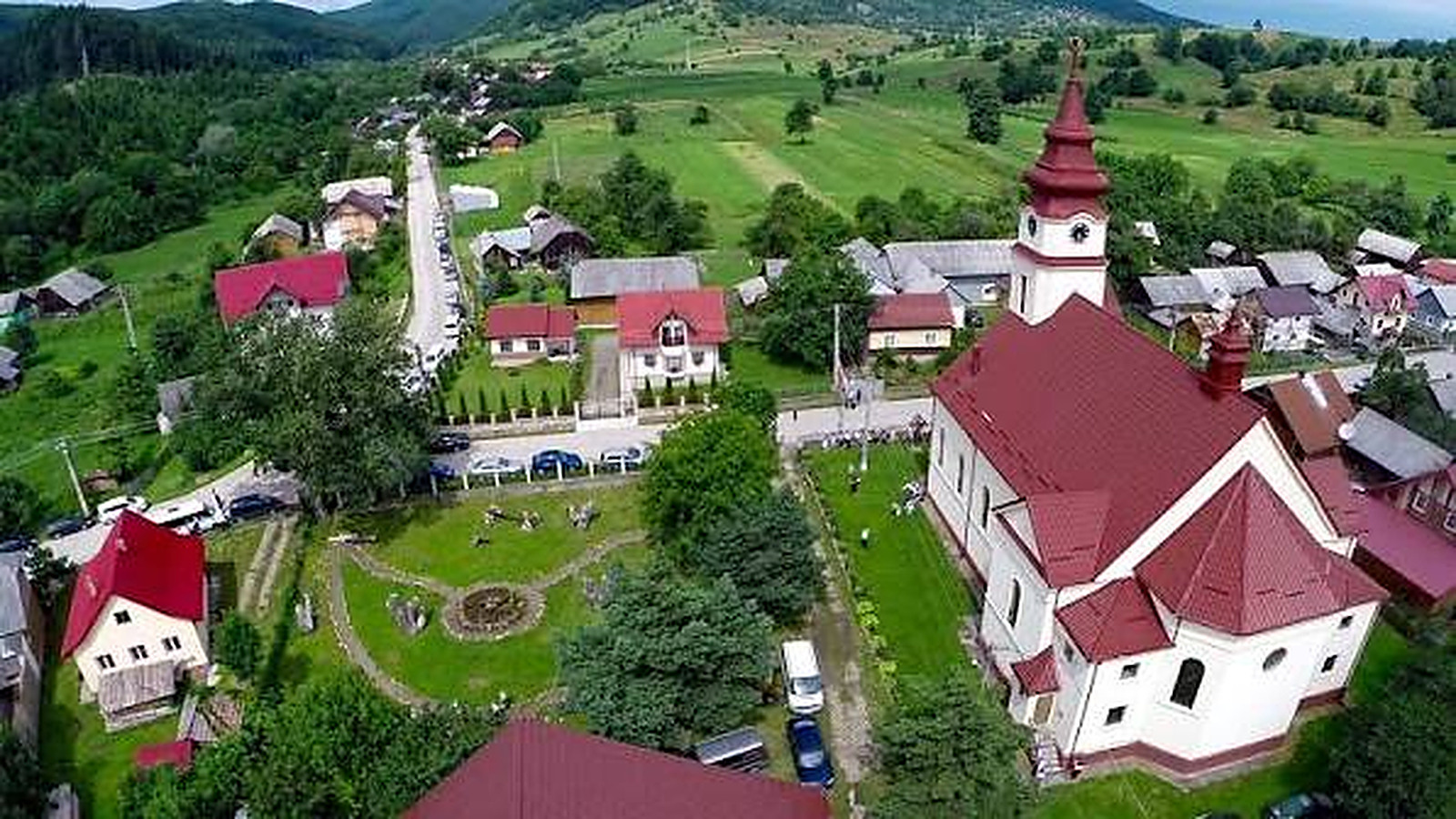 Widok z lotu ptaka na wieś z kościołem pośrodku, wśród pól i wzgórz